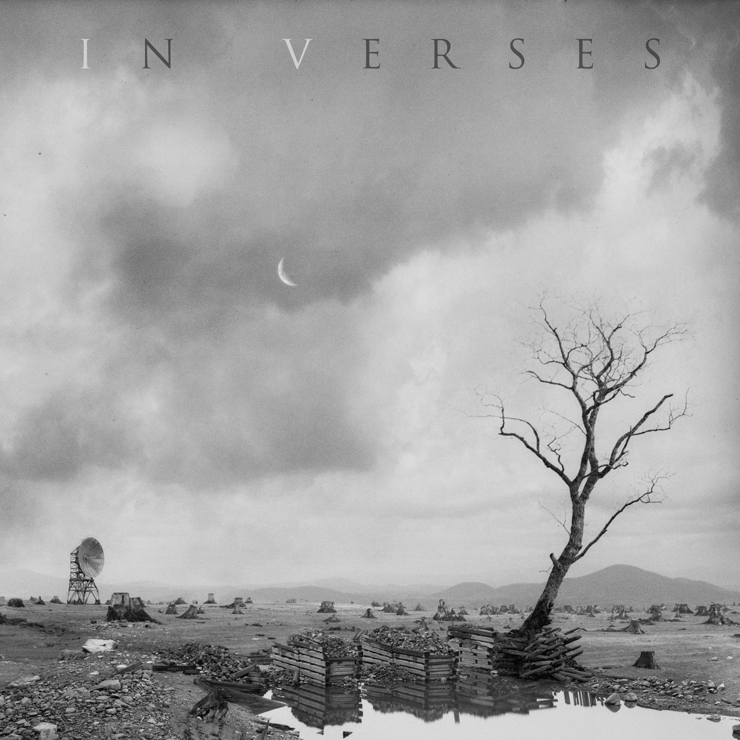 Cover of Karnivool's *In Verses* - a photo of a black-and-white wasteland full of tree stumps with a single leafless tree in the foreground by a pool of water. By the pool are some structures made of logs which are filled with rocks. In the background there's some kind of radio or sattelite dish. A crescent moon is visible over the clouds.